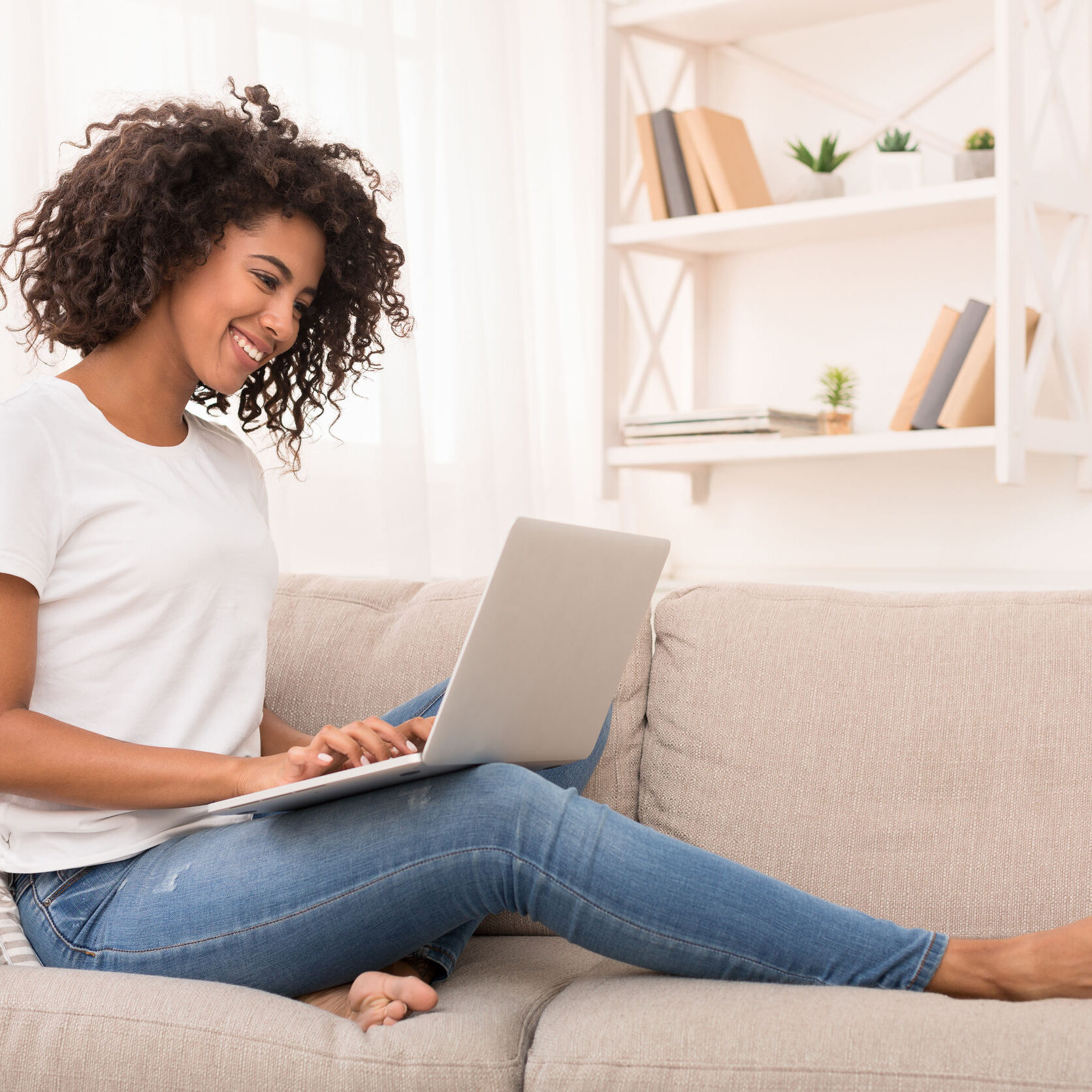 African-american woman working on laptop computer, sitting on sofa at home, copy space